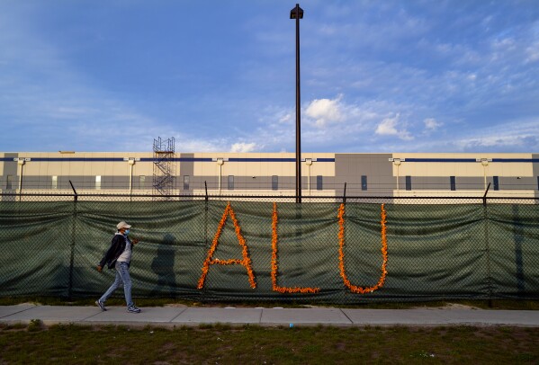 FILE - Letters representing Amazon Labor Union adorn a fence adjacent to the Amazon distribution center on Staten Island in New York on Oct. 25, 2021. Two years after clenching a historic union victory at the Amazon facility, the Amazon Labor Union is divided, running out of money and fighting over an election that could determine who will lead the group in the near future. (AP Photo/Craig Ruttle, File)