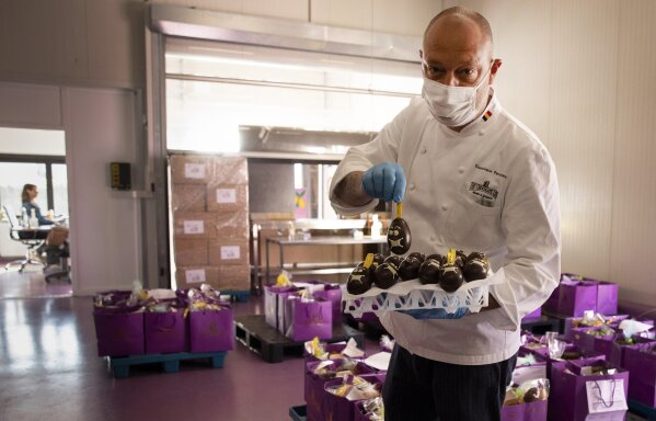 One of Belgium's top chocolate producers Dominique Persoone, wearing a face mask to protect against coronavirus, displays one of his chocolate Easter eggs at his Chocolate Line warehouse in Bruges, Belgium, Friday, April 10, 2020. As all non-essential shops in Belgium have been closed due to the outbreak of COVID-19, many chocolatiers have had to resort to online sales, home delivery or pick up on site. The new coronavirus causes mild or moderate symptoms for most people, but for some, especially older adults and people with existing health problems, it can cause more severe illness or death. (AP Photo/Virginia Mayo)