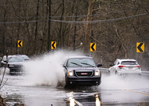 Vehicles splash through high waters on a flooded road in Schwenksville, Pa., Monday, Dec. 18, 2023. (AP Photo/Matt Rourke)