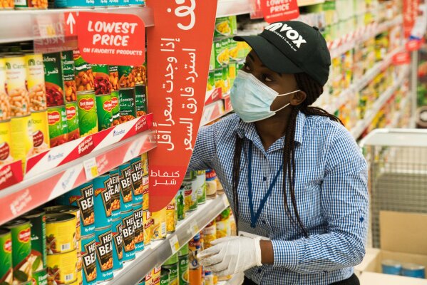 In this April 19, 2020 photo, Vox Cinema employee Jackline Nansamba of Uganda stocks shelves at a Carrefour supermarket while wearing a face mask amid the coronavirus pandemic in Dubai, United Arab Emirates. The coronavirus pandemic has exposed just how vital foreigners are to the Gulf Arab countries where they work as medics, drivers, grocers and cleaners. Vox Cinemas and Carrefour are both owned in the United Arab Emirates by the major retail firm Majid Al Futtaim. (AP Photo/Jon Gambrell)