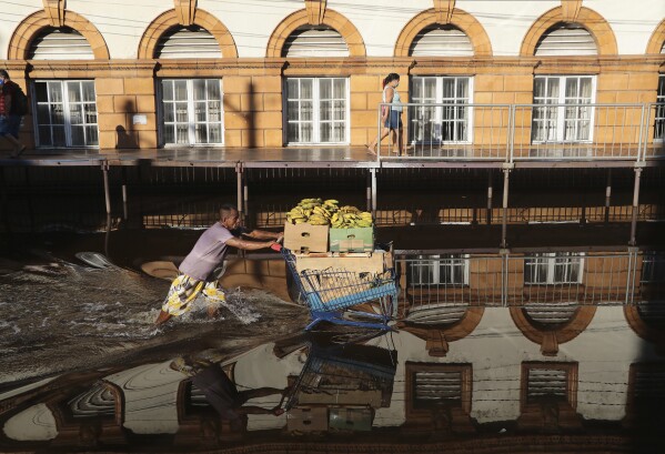 FILE - A man pushes a shopping cart loaded with bananas through a street flooded by the Negro River in downtown Manaus, Amazonas state, Brazil, on June 1, 2021. The Negro River has reached its lowest level on Monday, Oct. 16, 2023, since official measurements began. The record confirms the worst drought in this part of the world's largest rainforest, just a little over two years after its most significant flooding. (AP Photo/Edmar Barros, File)