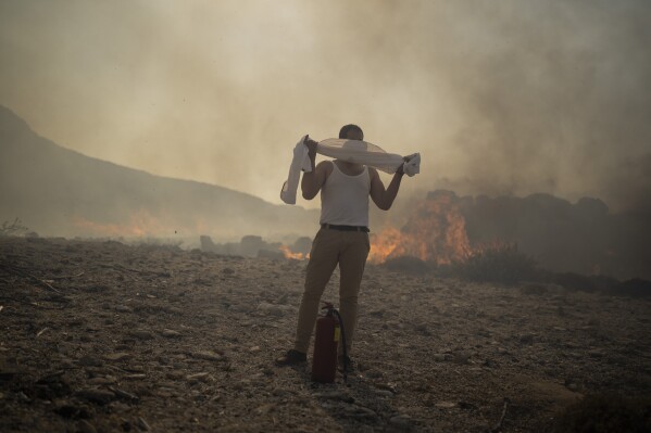 FILE - A man wraps his shirt over his face as he tries to extinguish a fire, near the seaside resort of Lindos, on the Aegean Sea island of Rhodes, southeastern Greece, on July 24, 2023. Europe is facing growing climate risks and is unprepared for them, the European Environment Agency said in its first-ever risk assessment for the bloc Monday, March 11, 2024. (AP Photo/Petros Giannakouris, File)