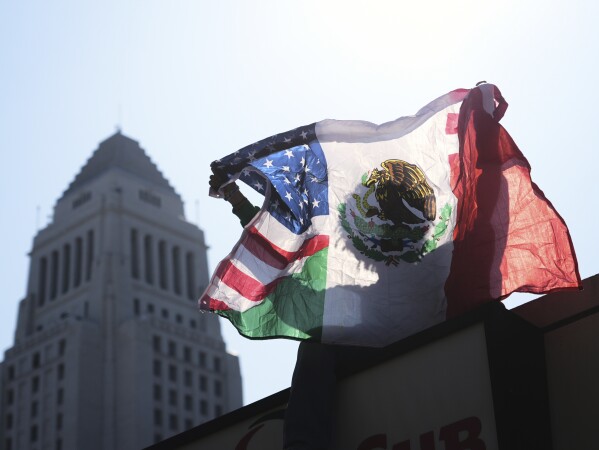 A person holds up an American and Mexican flag outside the Federal Building after federal immigration authorities conducted an operation Friday, June 6, 2025, in Los Angeles. (AP Photo/Damian Dovarganes)