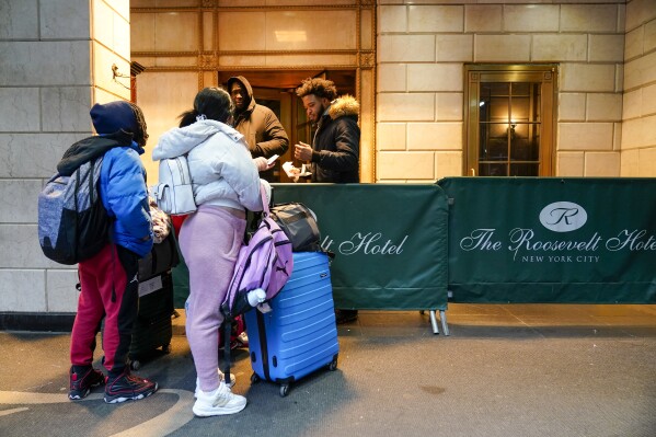 FILE - An immigrant family show their paperwork to security guards at the Roosevelt Hotel, Tuesday, Jan. 9, 2024, in New York. Hundreds of migrants are being evicted from New York City’s shelter system starting Wednesday, May 22, 2024, as part of a March settlement dealing with the city’s long standing “right to shelter” rule. (AP Photo/Mary Altaffer, File)