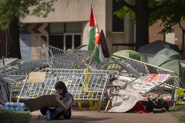 A person works on a sign board while sitting near a pile of barricades at an encampment by students protesting against the Israel-Hamas war at George Washington University on Tuesday, April 30, 2024, in Washington. (AP Photo/Mark Schiefelbein)