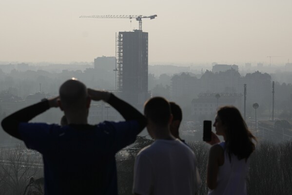 Athletes take a break as they run at the San Siro hill and look at the view skyline of Milan, Italy, Tuesday, Feb. 20, 2024. Italy's northern Lombardy region imposed severe antismog measures across Milan and eight surrounding provinces Tuesday to combat a particularly bad period of air pollution. The measures bar heavy motor vehicles from operating during the day and impose limits on heating and industiral agricultural activities in the nine provinces. (AP Photo/Luca Bruno)