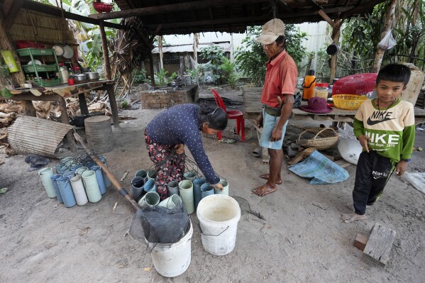 Chin Ith gathers palm sap collected from palm trees by her husband Chin Choeun, center, at Trapang Ampel village, outside Phnom Penh, Cambodia, Friday, March 15, 2024. Ith boils the sap over an open fire, stirring it until the right consistency of palm sugar is achieved. (AP Photo/Heng Sinith)