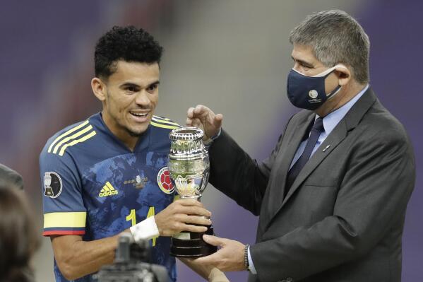 Conmebol General Secretary Jose Astigarraga, right, gives to Colombia's Luis Diaz the best player of the match trophy after beating 3-2 Peru in the Copa America soccer match for the third place at the National stadium in Brasilia, Brazil, Friday, July 9, 2021. (AP Photo/Andre Penner)