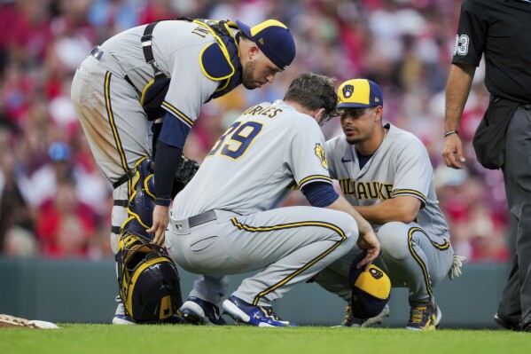Milwaukee Brewers' Victor Caratini, left, and Willy Adames, right, check on Corbin Burnes behind the pitcher's mound during the fifth inning of the team's baseball game against the Cincinnati Reds in Cincinnati, Friday, July 14, 2023. (AP Photo/Aaron Doster)