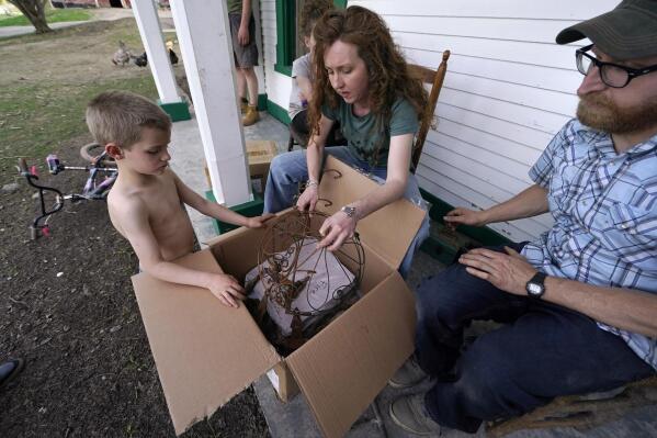 Ellie Holden, center, examines a box of "fire treasures", which are the burnt remains of their family's California home, with son Jack, left, and husband James, Thursday, May 12, 2022, in Proctor, Vt. After fleeing one of the most destructive fires in California, the Holden family wanted to find a place that had not been so severely affected by climate change and chose Vermont. (AP Photo/Charles Krupa)