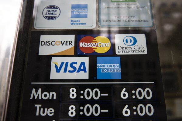 File - Credit card options are shown on a store's door on Nov. 29, 2018 in Philadelphia. Noticeable pockets of Americans are quickly running up their credit card balances and increasing numbers are now falling behind on their debts. (AP Photo/Matt Rourke, File)