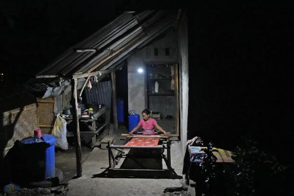 Tamar Ana Jawa is illuminated by a solar-powered light as she weaves a traditional cloth at a neighbor's house in Laindeha village on Sumba Island, Indonesia, Wednesday, March 22, 2023. Before electricity came to the village a bit less than two years ago, the day ended when the sun went down. Villagers in Laindeha, on the island of Sumba in eastern Indonesia, would set aside the mats they were weaving or coffee they were sorting to sell at the market as the light faded. (AP Photo/Dita Alangkara)