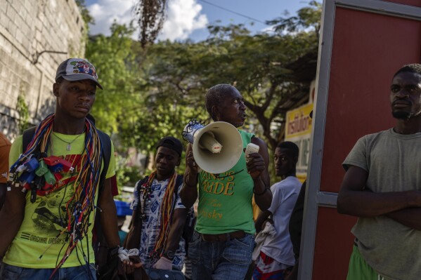A resident uses a loudspeaker to ask neighbors for a donation to pay for a metal gate to be installed as a barricade as protection against gangs, in the Petion-Ville neighborhood of Port-au-Prince, Haiti, Saturday, April 20, 2024. (AP Photo/Ramon Espinosa)