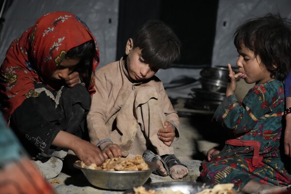 FILE - Afghan children eat in a makeshift shelter after an earthquake in Gayan district in Paktika province, Afghanistan, Saturday, June 25, 2022. About 6.5 million children in Afghanistan were forecast to experience crisis levels of hunger in 2024, a nongovernmental organization said Tuesday, May 29, 2024.(AP Photo/Ebrahim Nooroozi, File)