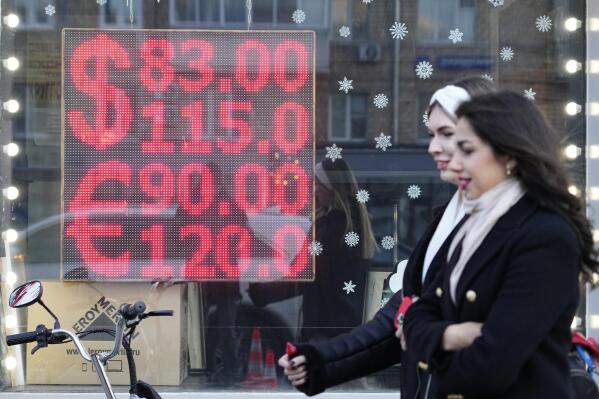 FILE - People walk past a currency exchange office screen displaying the exchange rates of U.S. Dollar and Euro to Russian Rubles in Moscow's downtown, Russia, Monday, Feb. 28, 2022. Russia's central bank cautiously reopened bond trading on the Moscow exchange Monday, March 21, 2022 for the first time since the country invaded Ukraine, with the price of Russia’s ruble-denominated government debt falling and sending borrowing costs higher. (AP Photo/Pavel Golovkin, File)