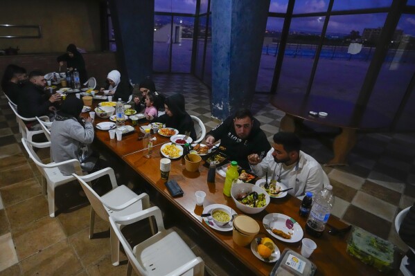 Residents displaced from their homes in southern Lebanon by clashes on the border with Israel eat during the Muslim's holy fasting month of Ramadan, at an abandoned hotel being used as a shelter in the southern town of Marwanieh, Lebanon, Friday, March 15, 2024. (AP Photo/Bilal Hussein)