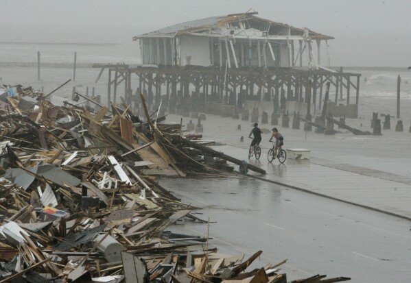 FILE - Cyclists ride past debris piled up on the seawall road after Hurricane Ike hit the Texas coast, Sept. 14, 2008, in Galveston, Texas. (AP Photo/Matt Slocum, File)