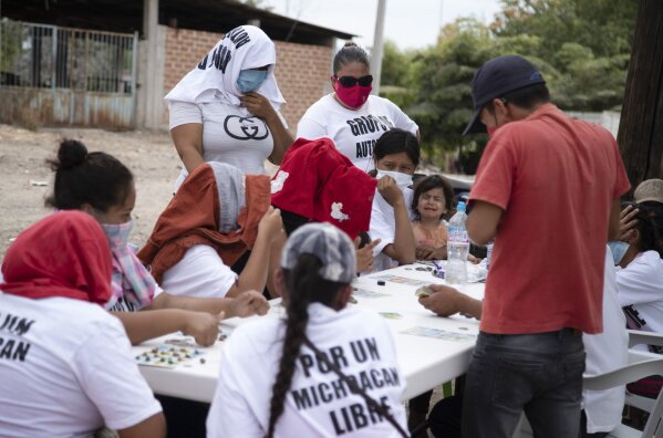 Women who say they are part of a female-led, self-defense group, some wearing T-shirts with a message that reads in Spanish: "For a free Michoacan,"  play board games at a check-point they set up to protect the entrance of their town of El Terrero, in Michoacan state, Mexico, Thursday, Jan. 14, 2021. Many of the women vigilantes in the hamlet of El Terrero have lost sons, brothers or fathers in the fighting. (AP Photo/Armando Solis)