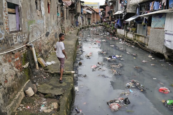 A boy walks along a polluted city canal at a lower-income neighborhood in Jakarta, Indonesia, Wednesday, March 13, 2024. (AP Photo/Dita Alangkara)