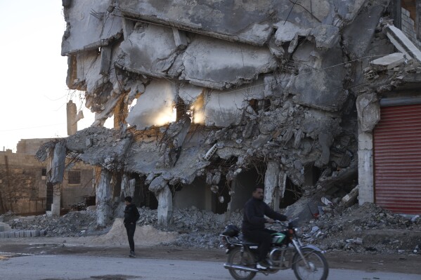 People pass by the house destroyed in the February 2023 earthquake in Jinderis, Syria, on Jan. 27, 2024. (AP Photo/Omar Albam)