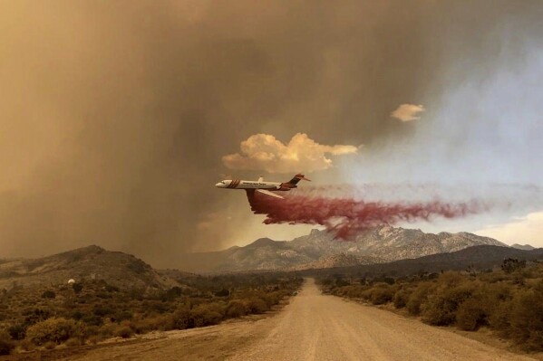 This photo provided by the National Park Service Mojave National Preserve shows a tanker making a fire retardant drop over the York fire in Mojave National Preserve on Saturday, July 29, 2023. A massive wildfire burning out of control in California's Mojave National Preserve is spreading rapidly amid erratic winds. Meanwhile, firefighters reported some progress Sunday against another major blaze to the southwest that prompted evacuations. (Park Ranger R. Almendinger/ InciWeb /National Park Service Mojave National Preserve via AP)