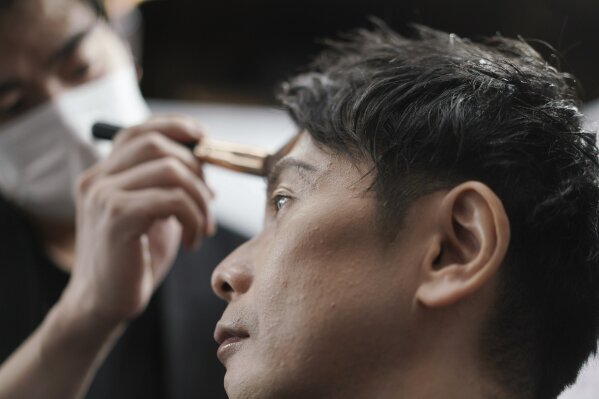 Yoshihiro Kamichi, a 44-year-old office worker, receives makeup and gets his hair done by a makeup artist at Ikemen-Works, a makeup salon for men, in Tokyo Wednesday, Feb. 3, 2021. The coronavirus pandemic has been pushing businesses to the edge in Japan, but some in the men's beauty industry have seen an unexpected expansion in their customer base. Japanese businessmen in their 40s, 50s and 60s who had little interest in cosmetics before the pandemic are now buying makeup. (AP Photo/Eugene Hoshiko)