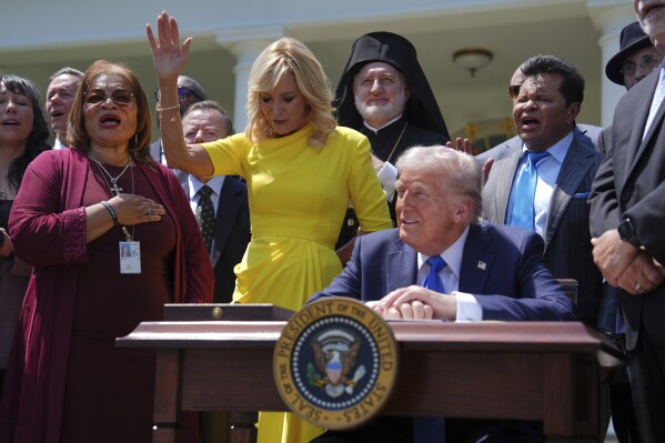 President Donald Trump sits at a desk as he and religious leaders listen to a musical performance before Trump signs an executive order during a National Day of Prayer event in the Rose Garden of the White House, Thursday, May 1, 2025, in Washington. (AP Photo/Evan Vucci)