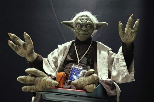 A Star Wars fan dressed as Yoda tries to look airborne during a fan convention called the Star Wars Celebration Japan in Chiba, near Tokyo, Friday, April 18, 2025. (AP Photo/Hiro Komae)