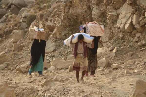 FILE - Yemenis carry relief supplies as they walk along a path after Shiite rebels, known as Houthis, besiege the city of Taiz, Yemen, Jan. 17, 2016. In a joint statement Monday, Aug. 29, 2022, sixteen rights groups urged Yemen’s Houthi rebels to end their years-long siege of Taiz, the country’s third-largest city. The groups, including Human Rights Watch and Amnesty International, said in a joint statement the Houthi blockade of Taiz has severely restricted freedom of movement and impeded the flow of essential goods, medicine, and humanitarian aid to the city’s residents. (AP Photo/Abdulnasser Alseddik, File)