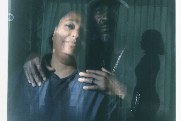 In this double exposure darkroom print made from two film negatives, a portrait of Krista Gwynn, left, and Navada, right, is layered with a portrait of their daughters, Navada, 15, left, and Victoria, 21, as they look out of the window of their home in Louisville, Ky., Tuesday, Aug. 29, 2023. Krista recalls that after their 19-year-old son, Christian, was killed in a drive-by shooting four blocks from home in 2019, her husband blamed himself for not doing more to protect him. Just two years later, Victoria, then also 19, was shot and injured at a park. Now the Gwynns have pulled their youngest child, Navada, out of school, home schooling to keep her safe. The two girls stay close to their parents and Victoria gets suspicious when cars slow down past their house. When the girls go out, Gwynn's husband insists on driving them, even to a friend's house blocks away. He carries a pistol for protection, pointing out that people, not their guns, are responsible for committing violence. 