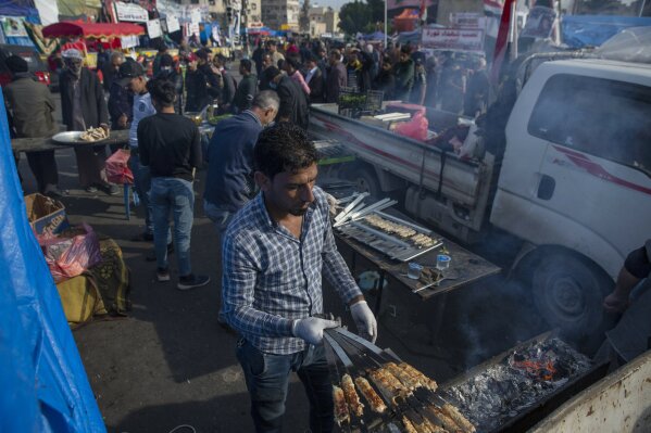 In this photo taken Thursday, Dec. 12, 2019, a volunteer chef serves free meals of the popular barbecue of Kabab, to Iraqi protesters at the center of Baghdad, Iraq.  In Baghdad’s Tahrir Square, there are the anti-government protesters demonstrating for a better future for Iraq, and there are the volunteers who feed them. From stuffed lamb and fish, to the giant pots of soups and rice to the plates of lentils and beans, there is no shortage of food to go around. Volunteers from the capital and southern provinces cook traditional dishes that reflect the country’s rich cuisine and bring protesters together.  (AP Photo/Nasser Nasser)