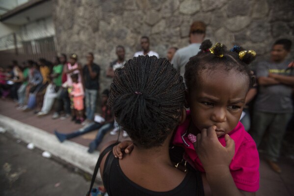 FILE - A Haitian woman carries her daughter as she waits outside the Mexican Commission for Migrant Assistance office, to get the documents needed that allow them to stay in Mexico, in Tapachula, early Thursday, June 20, 2019. Migrants, mostly from Haiti, have burst Monday, Sept. 18, 2023, into an asylum office in Tapachula, to demand papers. (AP Photo/Oliver de Ros, File)