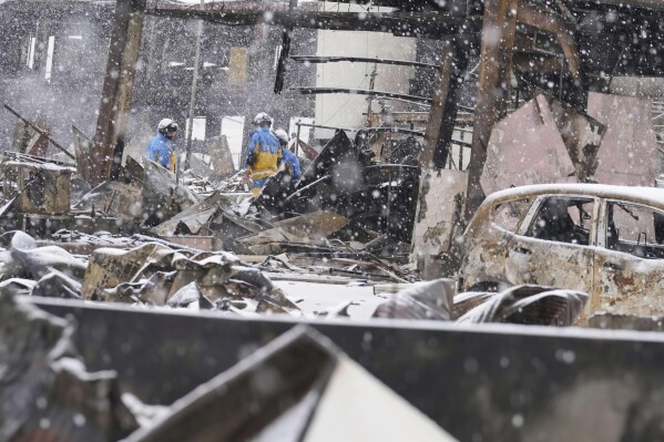 Snow falls as police officers continue a search operation around a burnt market in Wajima, Ishikawa prefecture, Japan Sunday, Jan. 7, 2024. A major earthquake slammed western Japan on Jan. 1, killing scores of people, toppling buildings and setting off landslides. (Kyodo News via AP)