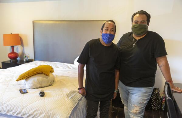 Homeless couple, Matthew Padilla, left, and Juan "Nito" Padilla. Jr., pose for a photo at their room in a hotel in Los Angeles Thursday, May 14, 2020. Anxiety mounted every time someone at the homeless shelter sneezed or residents got too close. For Matthew Padilla, a 34-year-old with a pacemaker and asthma, catching the novel coronavirus would likely mean death. So he jumped at the chance when his caseworker explained he could move into a hotel room for free as part of a new California program. Within days, he and his husband, Nito, were in a hotel room, where meals are delivered along with health screenings. (AP Photo/Damian Dovarganes)