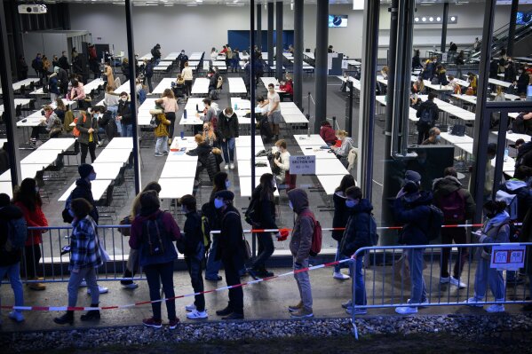 First-year students, wearing face masks to avoid the spread of the coronavirus, stand in line to enter in the building and prepare themselves, prior to a written exam at the SwissTech Convention Center of the Swiss Federal Institute of Technology site in Lausanne, Switzerland, Wednesday, Jan. 13, 2021. (Laurent Gillieron/Keystone via AP)