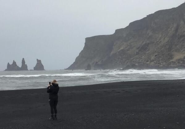 A tourist takes pictures on the volcanic black sand beaches of Vik, a coastal village in southern Iceland, March 29, 2017. After a summer of increased seismic activity, seismologists keep watch for volcanic activity, and there's an alert system to warn all 543 residents in Vik if the volcano blows, but there is no system to alert tourists who are flocking to Iceland’s waterfalls and geysers in record numbers.(AP Photo /Sheila Norman-Culp)
