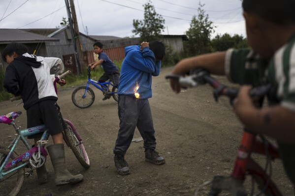 Joseph Phillip, 10, braces while igniting a firecracker with friends, Saturday, Aug. 19, 2023, in Akiachak, Alaska. Small firecrackers are for sale without age restriction from the Akiachak Enterprises general store. (AP Photo/Tom Brenner)