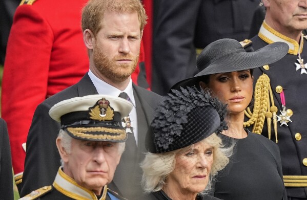 FILE - Britain's King Charles III, from bottom left, Camilla, the Queen Consort, Prince Harry and Meghan, Duchess of Sussex, watch as Queen Elizabeth II's coffin is placed in the hearse after the funeral of state at Westminster Abbey in central London on Monday, September 19, 2022. Queen Camilla, once seen as the scourge of the House of Windsor, the woman at the heart of King Charles III's doomed marriage to the The late Princess Diana has become one of the monarchy's most prominent emissaries.  (AP Photo/Martin Meissner, Pool, File)