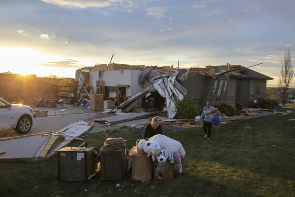 Two women help carry a friend's belongings out of their damaged home after a tornado passed through the area in Bennington, Neb., Friday, April 26, 2024. (AP Photo/Josh Funk)