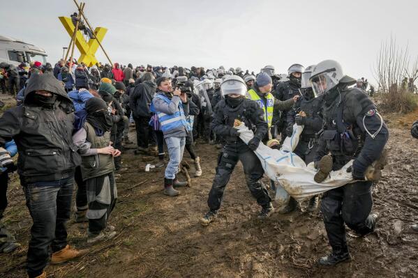 Police officers carry a demonstrator to clear a road at the village Luetzerath near Erkelenz, Germany, Tuesday, Jan. 10, 2023. The village of Luetzerath is occupied by climate activists fighting against the demolishing of the village to expand the Garzweiler lignite coal mine near the Dutch border. (AP Photo/Michael Probst)