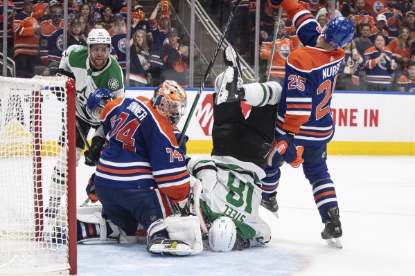 Dallas Stars' Sam Steel (18) is upended in front of the net as Edmonton Oilers goalie Stuart Skinner (74) makes a save during the third period of Game 4 of the Western Conference final in the NHL hockey Stanley Cup playoffs, Wednesday, May 29, 2024, in Edmonton, Alberta. (Jason Franson/The Canadian Press via AP)