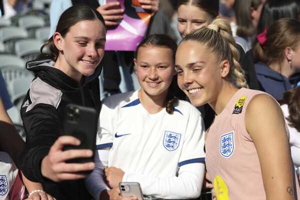 Matilda Gallagher, left, and Andie Chaseling, take a photo with England's goalkeeper Ellie Roebuck, right, at Central Coast Stadium in Gosford, Australia, Tuesday, July 25, 2023.England ranks second only to the United States in Women's World Cup ticket sales for countries outside of Australia and New Zealand. (AP Photo/Jessica Gratigny)