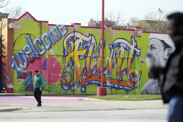 People walk by a mural in downtown Flint, Mich., Monday, March 25, 2024. (AP Photo/Carlos Osorio)