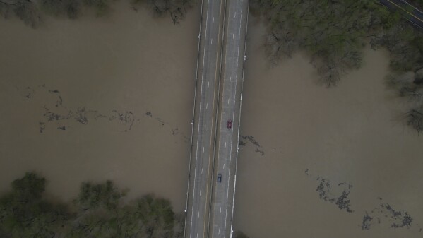 An aerial view of debris floating down the Kentucky River as vehicles drive over a bridge Saturday, April 5, 2025, in Frankfort, Ky. (AP Photo/Jon Cherry)