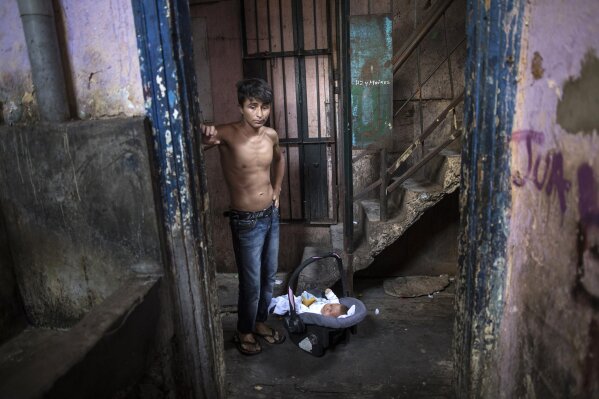 In this April 3, 2020 photo, ex-convict Julio Ramos stands next to his 3-month-old son Jose, inside the deteriorating building where he lives nicknamed “Luriganchito” after the country’s most populous prison, in Lima, Peru. “I do not want my children to suffer as I did, I want to give them the love I never had”, said the 26-year-old father of 3 boys. (AP Photo/Rodrigo Abd)