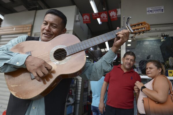 Street musician Angel Alvarado, known as "Allan El Trovador," sings his "coronavirus" song at a market in Guayaquil, Ecuador, Tuesday, March 3, 2020. Alvarado, from Colombia, said he started improvising songs about the coronavirus that includes people's complaints about price gouging in Guayaquil, a city where several patients are being treated with for COVID-19. (AP Photo/Marcos Pin)
