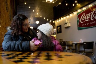 In this Jan. 24, 2020, photo, Mary Oldham, 27, a middle school science teacher from Knoxville, Iowa poses for a photograph with her daughter Kailyn, 6, at Smokey Row Coffee, in Pella, Iowa. Oldham was never much into politics but says her boyfriend has gotten her thinking: If you don’t vote, you don’t have a voice. So Oldham is planning to caucus Monday, Feb. 3 — for a Democrat. (AP Photo/Andrew Harnik)