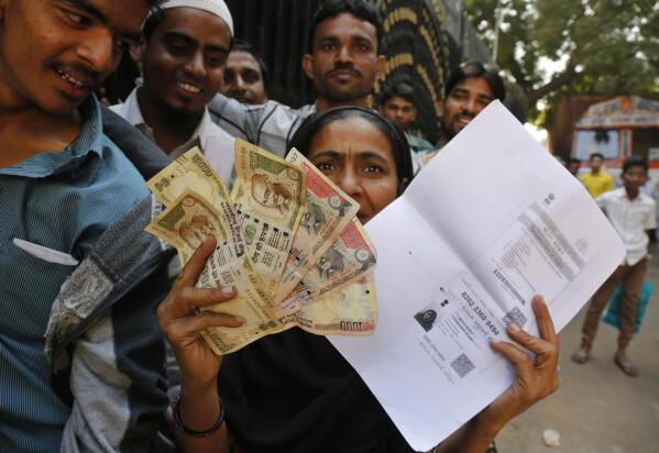 FILE- An Indian woman shows discontinued Indian currency notes and copy of photo identity card as she stands in queue outside Reserve Bank of India to deposit and exchange them in Ahmedabad, India, Nov. 17, 2016. In November 2016, India withdrew all 500-rupee and 1,000-rupee from circulation, in an effort to tackle corruption, black money and tax evasion. India’s top court hearing petitions challenging the currency ban on Monday, Jan.2. 2013 said the government’s surprise decision in 2016 to demonetize high-value bills was legal and taken after consultation with India's central bank. (AP Photo/Ajit Solanki, File)