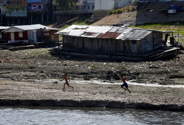 FILE - Boys walk next to a floating home stranded on what used to be the water's edge of the Negro River, amidst a drought in Manaus, Brazil, Sept. 26, 2023. The extreme drought sweeping across Brazil’s Amazon rainforest is already impacting hundreds of thousands of people and killing local wildlife. (AP Photo/Edmar Barros, File)