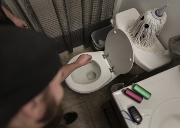 Tyler Baker flushes fentanyl as his peer support worker Jesse Johnson of the Family Resource Center stands at left, in Findlay, Ohio, Thursday, Oct. 12, 2023. After talking with Johnson, Baker, an active user, agreed to dispose of his supply of fentanyl. (AP Photo/Carolyn Kaster)